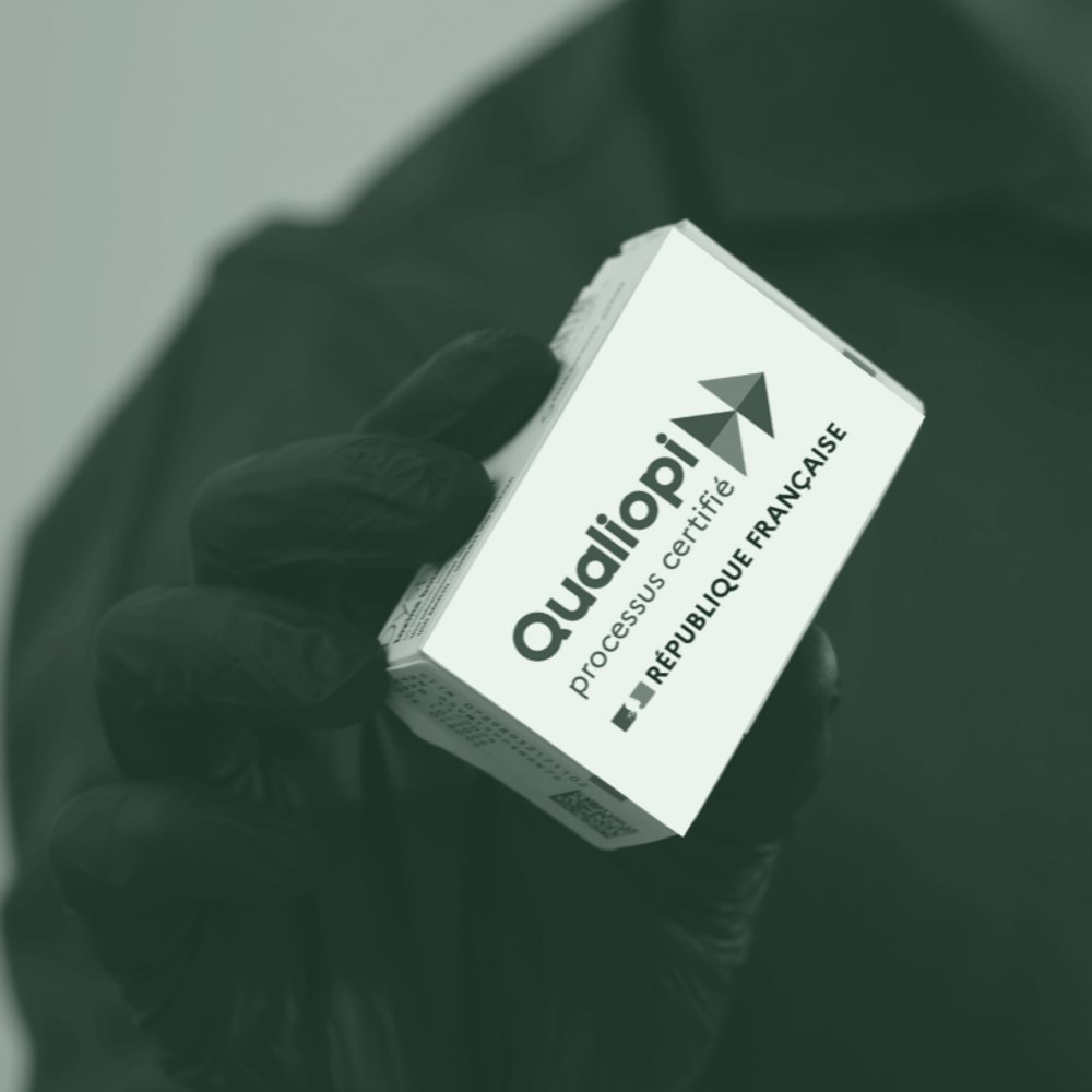 Main gantée tenant une boîte façon médicament portant le logo Qualiopi, processus certifié.