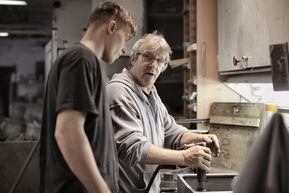 Le père montre une pièce à son fils à l'établi de l'atelier, outil en main